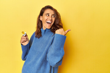 Pregnant woman with pacifier on yellow studio points with thumb finger away, laughing and carefree.
