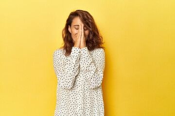 Middle-aged woman on a yellow backdrop holding hands in pray near mouth, feels confident.