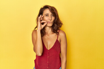 Middle-aged woman on a yellow backdrop with fingers on lips keeping a secret.