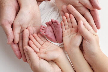 The palms of the father, the mother are holding the foot of the newborn baby in a white blanket. Feet of the newborn on the palms of the parents. Studio macro photo of a child's toes, heels and feet.