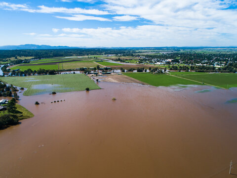 Brown floodwaters backflowing over farmland in Singleton