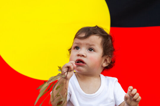 First Nations Australian child looking up against aboriginal flag backdrop