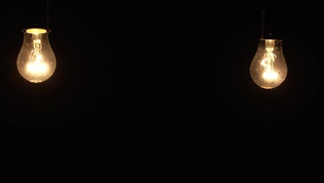 Two light bulbs hanging and swinging on a black background