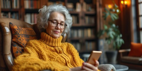 A smiling senior grandmother enjoys modern technology, sitting comfortably at home using her phone.