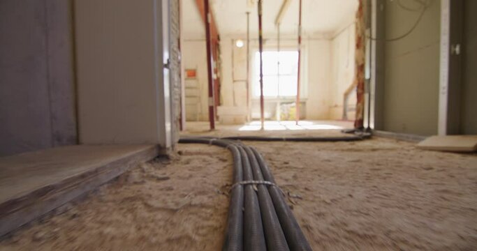 Low angle shot of following electric cables running on the floor on a construction site, entering a room with huge windows.