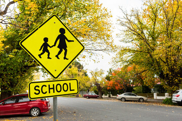 Bright yellow school sign in Autumn street with parked cars