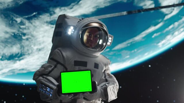 Astronaut Holding a Tablet Computer with Green Screen Mock Up Display in Landscape Mode in Outer Space. Space Technology and Exploration Template Concept for Advertising and Marketing Campaigns