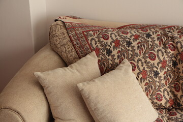 beige sofa and pillows with ethnic patterned shawl. paisley shawl placed on the sofa. Minimalist home decor. 