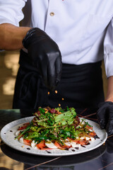 The cook sprinkles pine nuts on Caesar salad