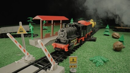 Model of a children's plastic steam train with freight cars and ferry rides along the tracks and...