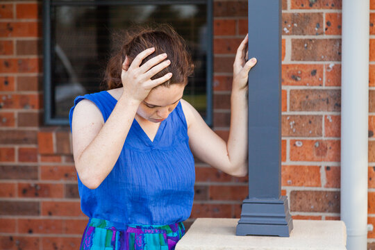 Concept - vertigo, spinning, dizziness. Woman leaning on post outside home to stay upright