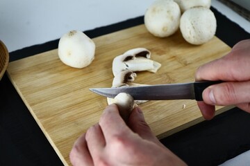 Male hands cutting champignons on a wooden board