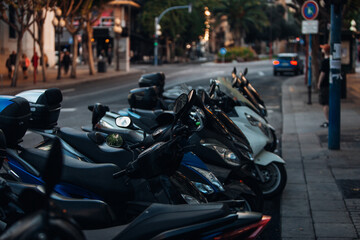 A group of motor scooters parked on the street of a European city in the evening