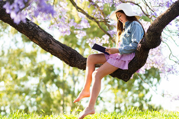 Barefoot girl reading a novel in tree after school
