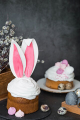 Beautiful stylish still life. Easter cake with rabbit ears, meringue, marshmallows, Easter eggs and willow twigs on a dark background. happy Easter 2024.