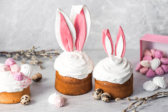 Beautiful stylish still life. Easter cake with rabbit (hare) ears, meringue, marshmallows, Easter eggs and willow branches and on a light concrete background. Happy Easter 2024.