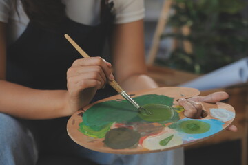 Cropped image of female artist standing in front of an easel and dipping brush into color palette
