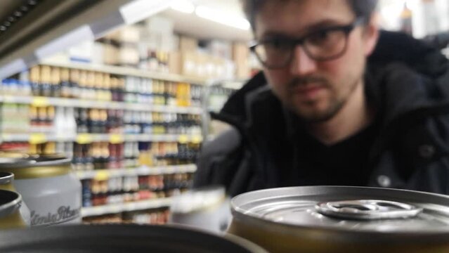 Many beer cans in a supermarket refrigerator and a man with a shopping trolley takes a couple
