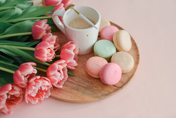 Bouquet of pink tulips, cup of coffee and macaroons on pink background. Anniversary celebration concept. Copy space. Top view