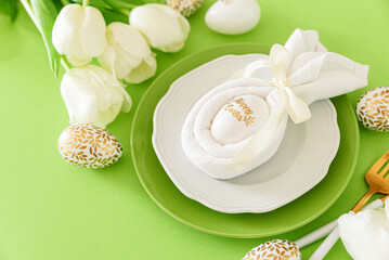 Plate decorated bunny ear napkin, white tulips and Easter eggs on green background. Easter celebration concept. Flat lay. Top view