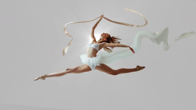 rhytmic gymnastics jump on split with ribbon isolated in grey studio 
