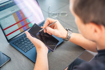 Close up view of man hand holding smart phone and stylus pen at his creative workspace. 