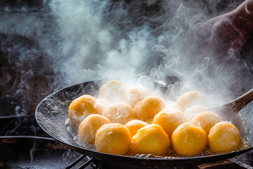 Close-up of a frying pan where fritters are being fried and cooked. Typical Easter and Carnival sweets. - obrazy, fototapety, plakaty