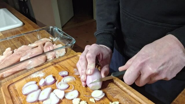 Slice peeled onions into rings. A man cuts a peeled onion on a wooden cutting board. Preparing chicken cutlets for baking in the kitchen oven. Concept of cooking and culinary