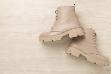 Beige trendy boots on wooden background, top view.