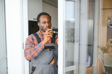 Workman in overalls installing or adjusting plastic windows in the living room at home