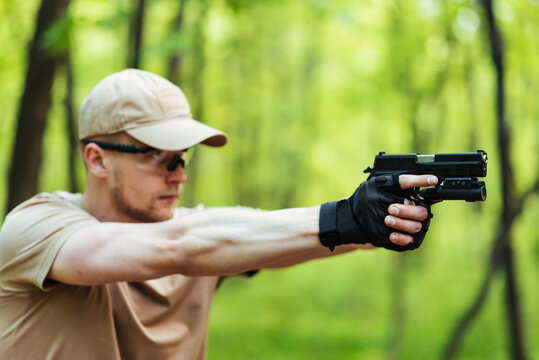 instructor with gun in forest leads aiming and posing on camera