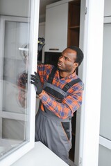 Workman in overalls installing or adjusting plastic windows in the living room at home