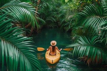 Amidst the lush green jungle, a fearless woman navigates the winding river in her vibrant yellow kayak, gliding gracefully through the tranquil waters with her trusty paddle as her only means of tran - obrazy, fototapety, plakaty