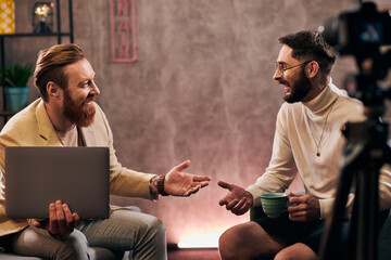 two joyful handsome men in elegant attires with coffee and laptop discussing interview questions