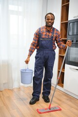 Professional cleaner in blue uniform washing floor and wiping dust from the furniture in the living room of the apartment. Cleaning service concept