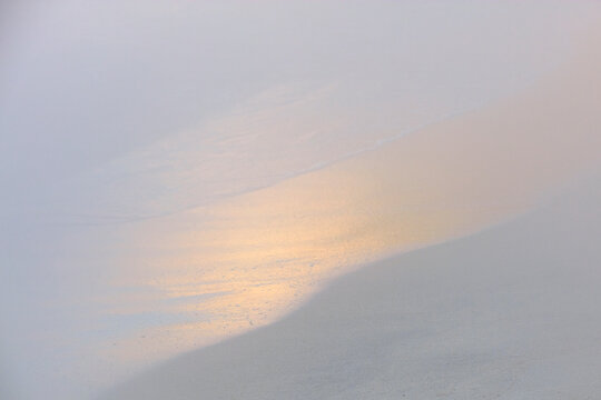 Minimalist image of a subtle sand gradient with the gentle gleam of a sunset reflected on the shore