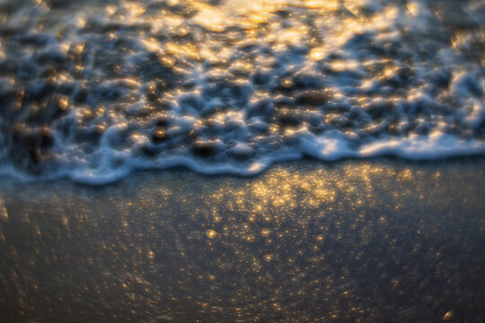 Golden sunlight dances on the sea's surface, creating a sparkling texture as waves gently lap the shore