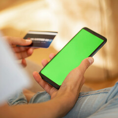 Close up of smartphone with green screen and bank card in female hands. Online shopping or payment.