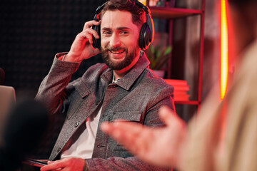 handsome cheerful man in casual cozy attire sitting with laptop in studio next to his podcaster