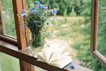Beautiful summer still life on the windowsill. A bouquet of cornflowers and a book on the...