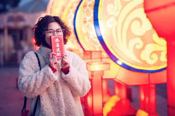 Woman holding red envelope under lanterns at Spring Festival temple fair