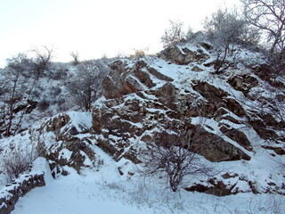 A view from below on the steep Dnieper rocks that hide safe passages under the cover of snow against the background of a clear frosty sky.