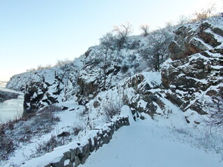 A view from below on the steep Dnieper rocks that hide safe passages under the cover of snow against the background of a clear frosty sky.