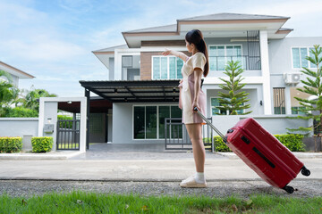 A young Asian woman with luggage standing in front of a new buying home to move into a new house....