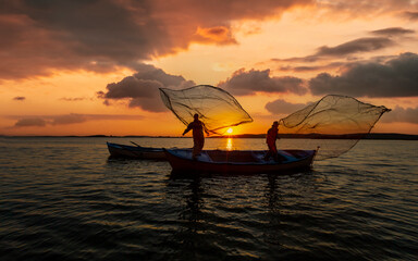 Silhouette of fishermen with yellow and orange sun in the background
