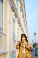 Traveler asian woman in her 30s using smartphone to take a photo while traveling urban street in Bangkok, Thailand