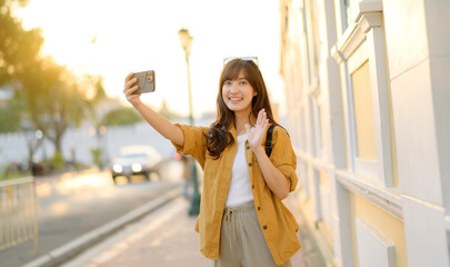 Fototapeta premium Traveler asian woman in her 30s making a livestream and selfie with a smartphone enjoying travel in Bangkok, Thailand. Journey trip lifestyle, world travel explorer or Asia summer tourism concept.