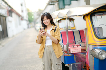 Young Asian woman backpack traveler standing a side of Tuk Tuk taxi on summer vacations at Bangkok, Thailand. Journey trip lifestyle, Asia summer tourism concept.