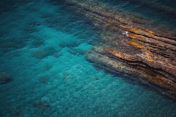 Aerial view of calm turquoise sea water and rocks from molten lava from drone. Pattern of sea...