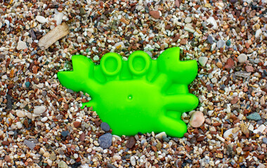 Children's plastic green toy sand mold in the shape of a crab close-up against a background of pebbles on the beach
